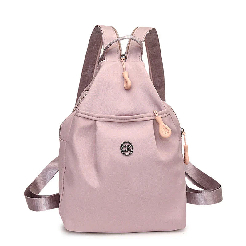Bolso convertible de hombro: vista frontal de una mochila pequeña color rosa polvoriento con correas para los hombros, asa superior, múltiples tiradores de cremallera e insignia central con logotipo