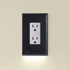 An outlet cover with integrated led night guidelight is mounted on a light beige wall, with soft LED light glowing from its bottom edge.