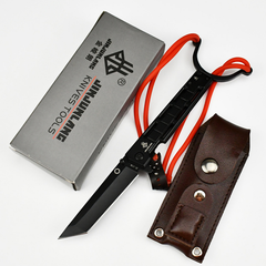 An EDC folding knife with attached slingshot parts, a brown leather sheath, and a branded product box laid on a white background.