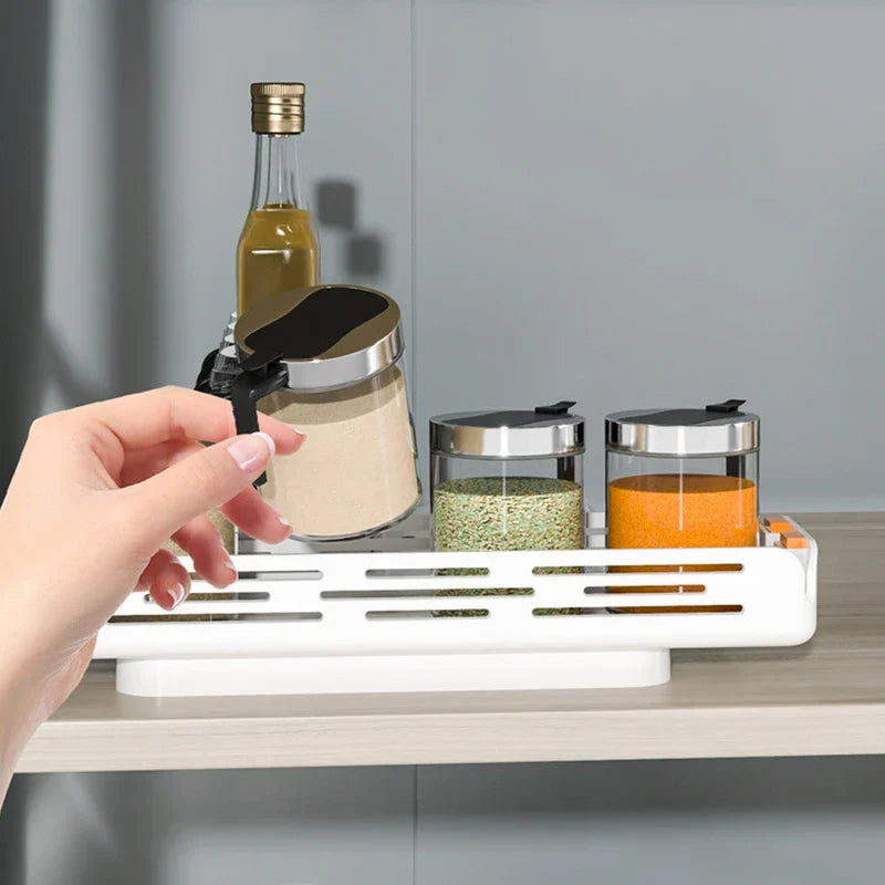 doppellagiges aufbewahrungsregal - Eine Hand hebt ein Glasgewürzglas von einem weißen Regal auf der Arbeitsplatte, das weitere Gewürzbehälter und eine kleine Ölflasche enthält