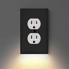 An outlet cover with integrated led night guidelight is mounted on a dark gray wall, with warm LED light glowing downward from its bottom edge.