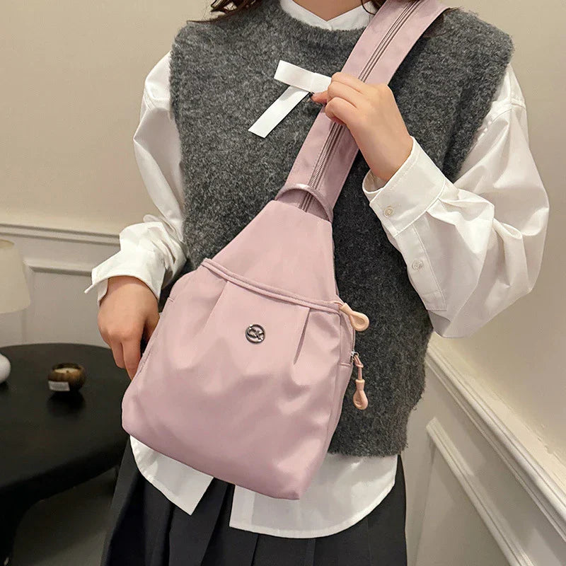 Bolso convertible de hombro: vista frontal de una persona con camisa blanca y chaleco gris sosteniendo la correa de un bolso convertible cruzado/mochila rosa claro sobre el hombro