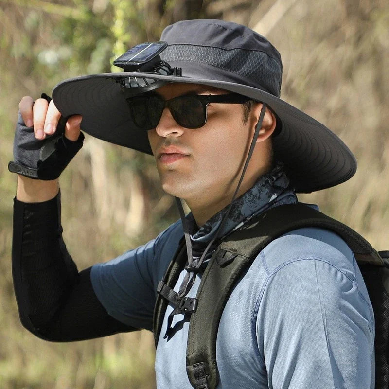 sombrero de ala ancha - Hombre con equipo de exterior usando un sombrero de ala ancha oscuro con ventilador solar montado, gafas de sol, guante de medio dedo, cuello de braga y correa de mochila, sosteniendo el ala del sombrero en un entorno natural al aire libre
