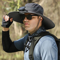 sombrero de ala ancha - Hombre con equipo de exterior usando un sombrero de ala ancha oscuro con ventilador solar montado, gafas de sol, guante de medio dedo, cuello de braga y correa de mochila, sosteniendo el ala del sombrero en un entorno natural al aire libre