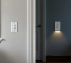 White outlet cover with integrated led night guidelight mounted on hallway wall, one unit emitting warm downward glow