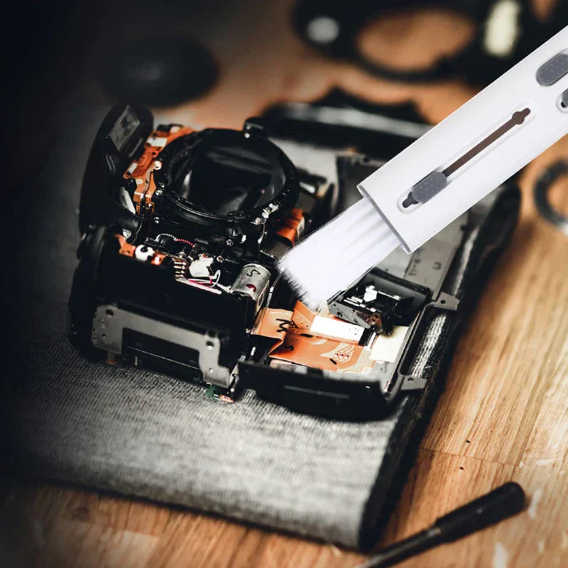 White cleaning brush being used to dust internal camera components on a work surface