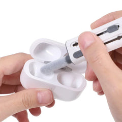 Hands use a fluffy tipped white cleaning tool to clean an open white wireless earbud charging case; no visible keyboard cleaning brush.
