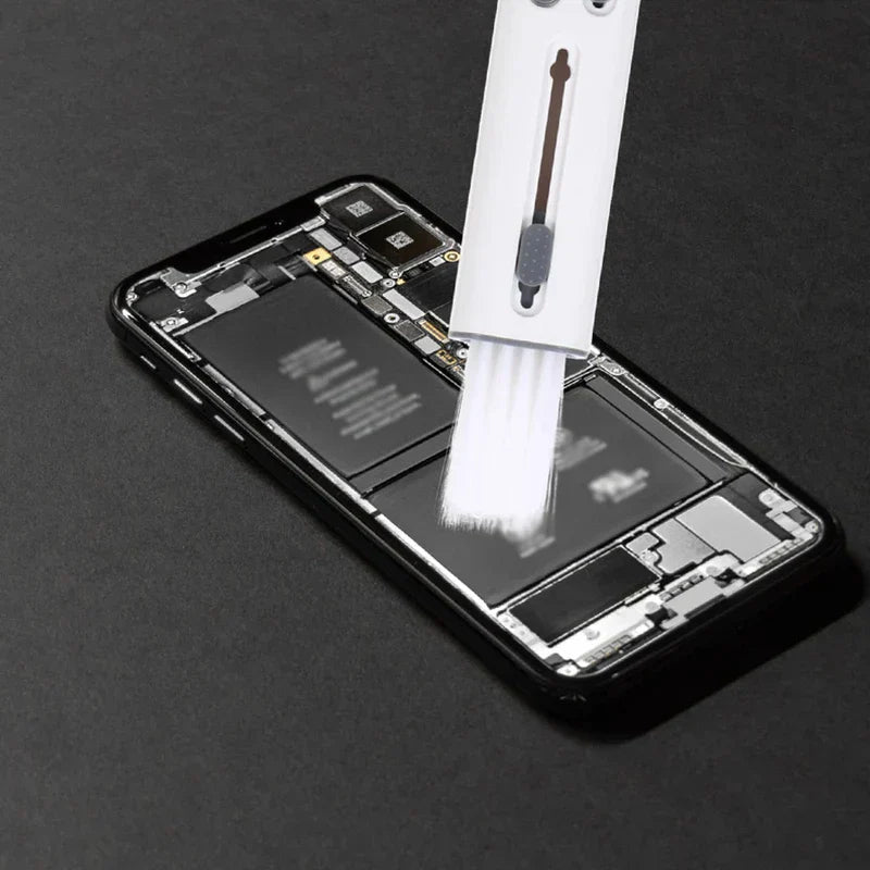 A keyboard cleaning brush is held above an opened smartphone's internal components.