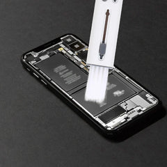 A keyboard cleaning brush is held above an opened smartphone's internal components.