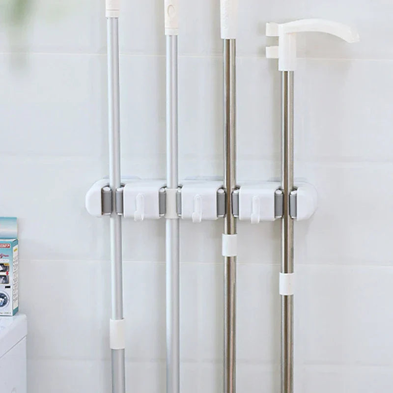 soporte de pared para trapeador y escoba - Organizador de pared con 4 ranuras montado en una pared de azulejos blancos, sosteniendo cuatro herramientas de limpieza de mango largo