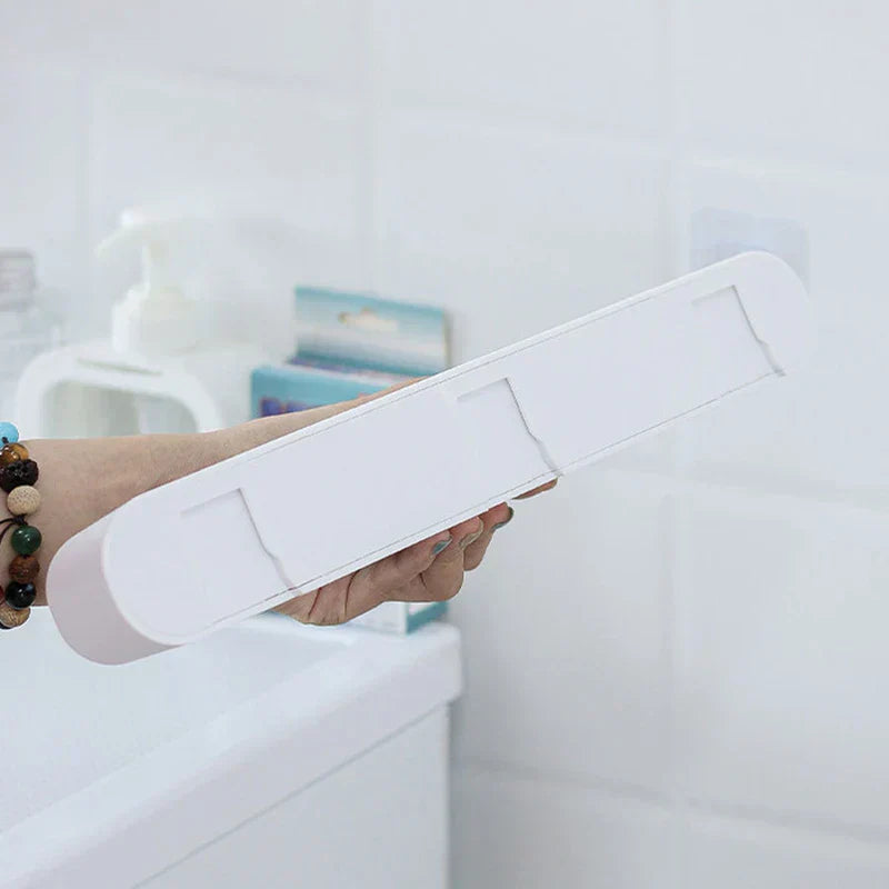 soporte de pared para trapeador y escoba - Mano sosteniendo una tira de montaje larga de plástico blanco con tres pestañas adhesivas, en un entorno de baño
