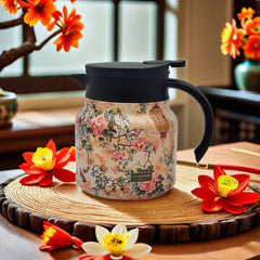 Vintage Floral Tea Thermos - Insulated teapot with floral and lantern pattern, black lid and handle, resting on a wooden slice trivet surrounded by artificial flowers.