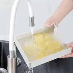 Vegetable Slicer Chopper - Hands holding white produce tray with waffle-cut potato slices under running kitchen faucet