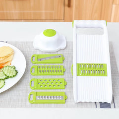 Vegetable Slicer Chopper - slicer body, food holder, and four blade inserts arranged on linen mat with plate of cut vegetables to the side