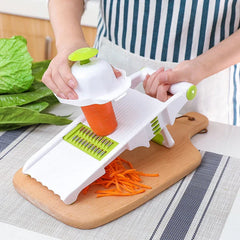 Vegetable Slicer Chopper - Person slicing a carrot into thin strips with a white and green mandoline slicer set on a wooden cutting board