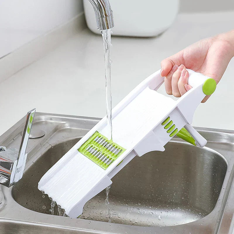 Vegetable Slicer Chopper - A hand holds a white and green vegetable slicer under running water in a stainless steel sink for cleaning