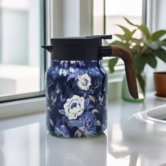Vintage Floral Tea Thermos - Insulated pitcher with dark blue floral print, black lid, wood-grain handle, on a white windowsill with green plant behind