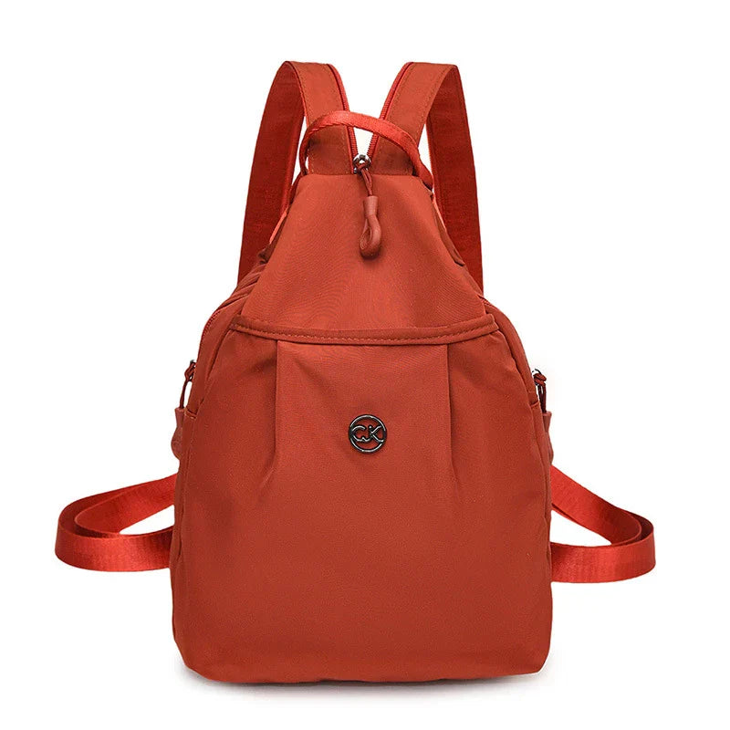 Bolso convertible de hombro: vista frontal de una mochila pequeña color terracota con correas para los hombros, asa superior y insignia central con logotipo