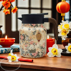 Vintage Floral Tea Thermos - Insulated pitcher with light beige traditional floral and lantern print, black lid, wood-grain handle, on a wooden table with candles and daffodils
