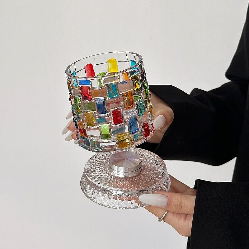 vaso de cristal para whisky - Una persona sostiene un vaso corto con patrón tejido multicolor sobre su base de vidrio texturizado transparente con un disco metálico plateado