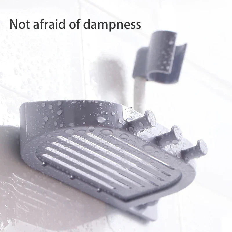 Shower Head Holder - Grey wall-mounted soap dish with hooks and a curved hose clip, covered in water droplets, against a wet tiled surface.
