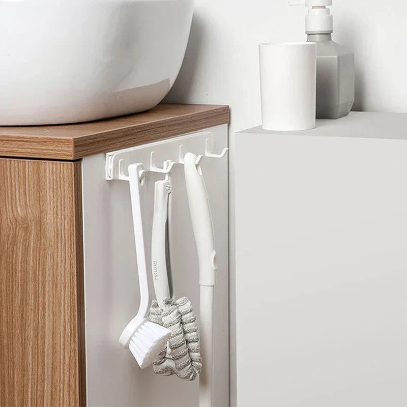 Wall Hook Hanger - White hook rack with 5 hooks mounted on the side of a bathroom vanity under a sink, holding three cleaning brushes with white handles