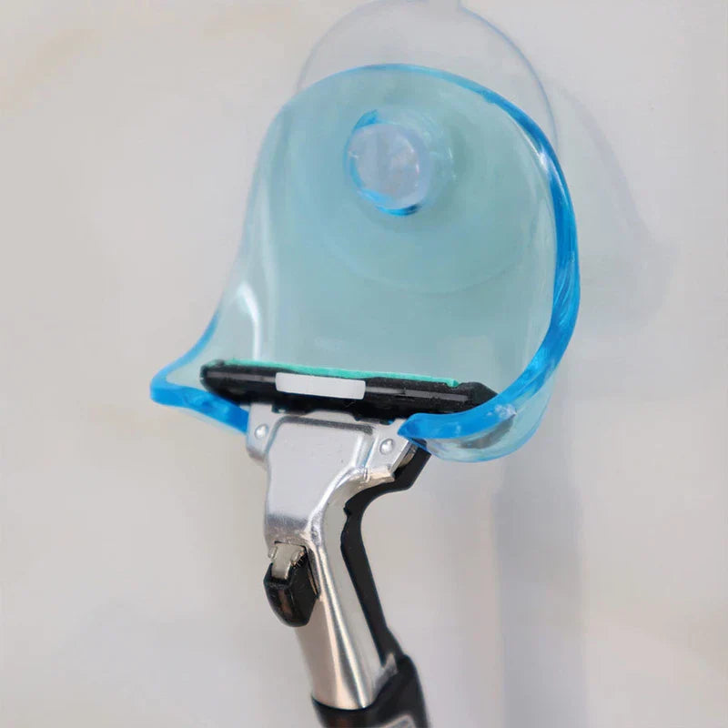 Soporte de pared adhesivo con ventosa para maquinilla de afeitar - soporte para maquinilla con ventosa en azul translúcido montado en una pared clara, sosteniendo una maquinilla manual plateada y negra