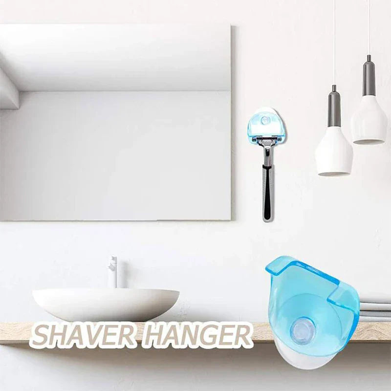 Soporte de pared adhesivo con ventosa para maquinilla de afeitar - escena de baño con lavabo, espejo y dos luces colgantes. Una maquinilla está sostenida por un soporte con ventosa azul en la pared, y el texto "COLGADOR DE MAQUINILLA" aparece cerca del lavabo