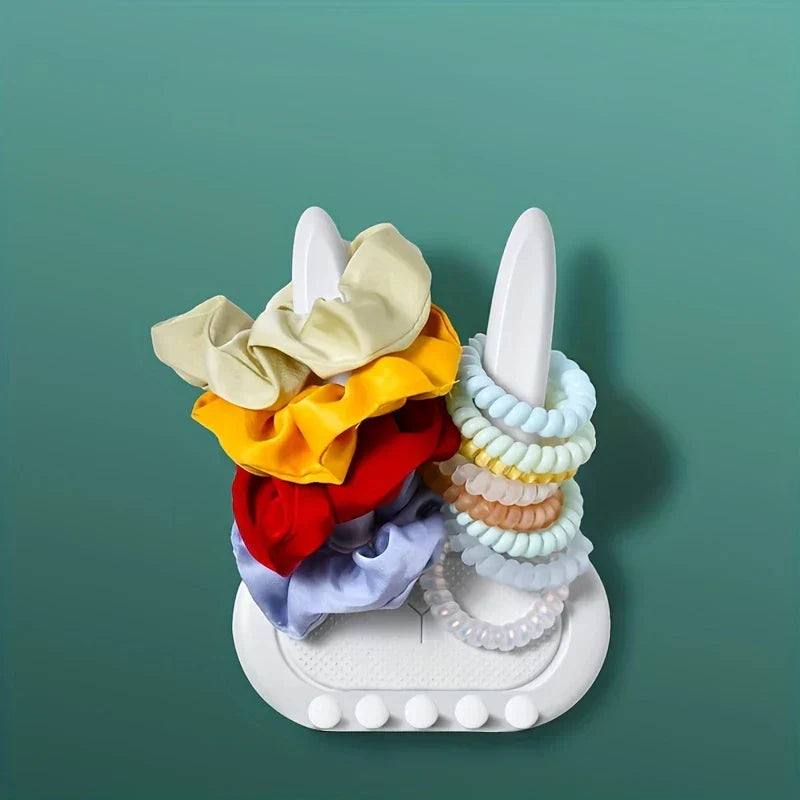 Utility Hooks - White rabbit-shaped organizer with scrunchies on one ear and spiral hair ties on the other, against teal background.