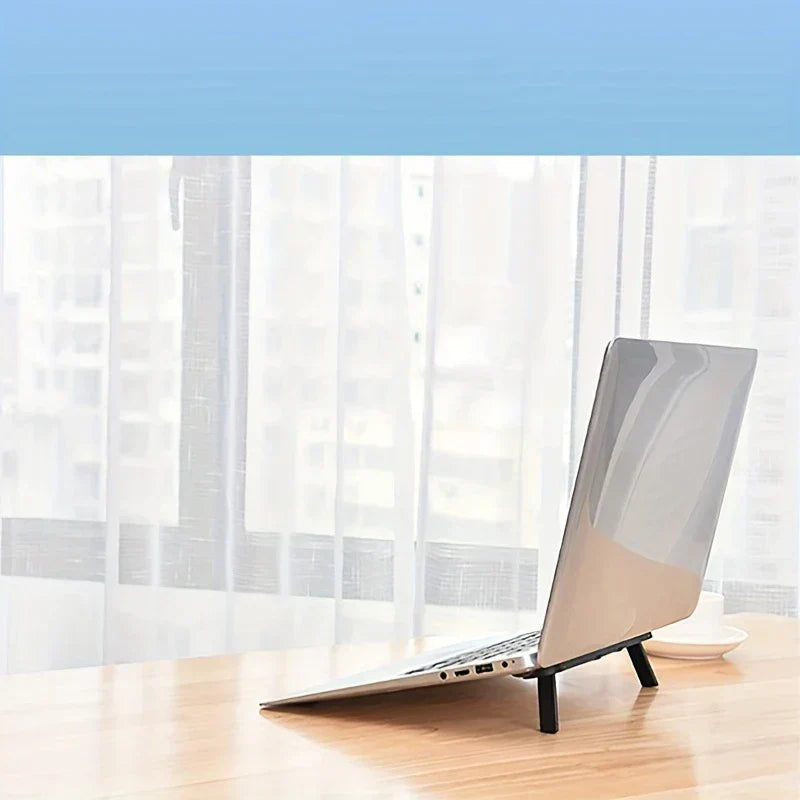 Portable Laptop Stand - Silver laptop propped on small stand on wooden desk near sheer curtains