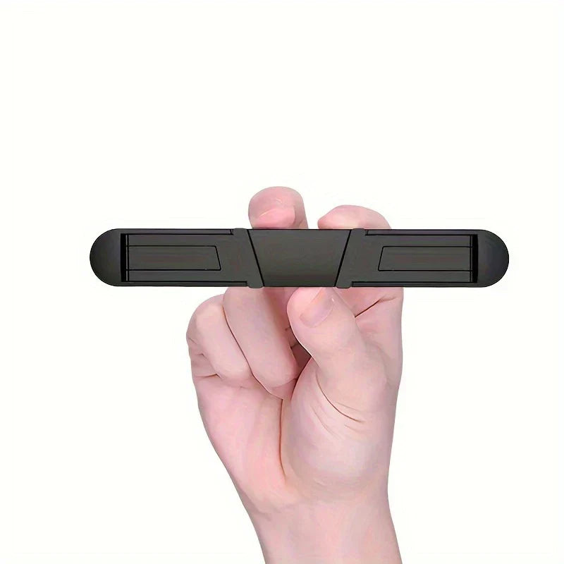 Portable Laptop Stand - A hand holds a small black elongated folding device horizontally, showing its folded flat state against a white background