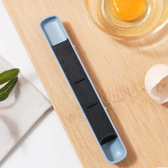 Adjustable Measuring Spoon - Light blue and black graduated double-ended measuring scoop on a wooden cutting board, beside a raw egg in a glass bowl and egg shell.