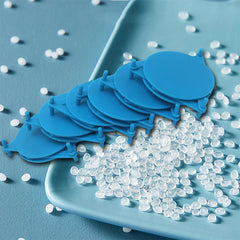 Shelf Organizer Rack - A stack of blue circular plastic clips with prongs rests on a light blue tray scattered with clear plastic pellets