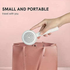 cepillo desenredante para el cabello - mano sosteniendo un cepillo blanco de mano sobre un bolso de piel rosa, texto 'PEQUEÑO Y PORTÁTIL viaja contigo' sobre fondo rosa claro