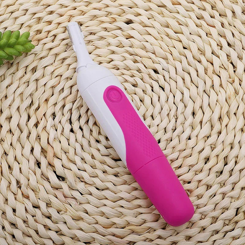 Facial Tool - Pink and white electric trimmer with narrow trimmer head attached, resting on woven rattan mat with small green plant at top left