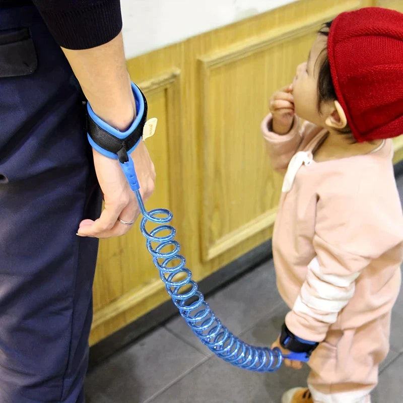 Wrist Link - Adult and toddler wearing connected blue coiled wrist leashes, standing near a wooden wall indoors