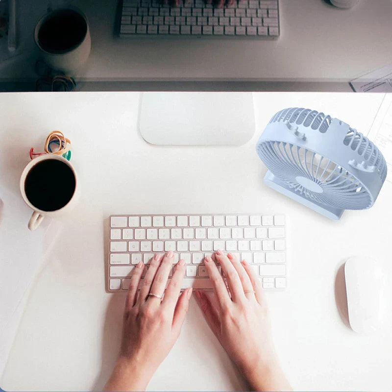 tischventilator - Draufsicht auf Hände, die auf einer Tastatur tippen, mit einem hellblauen USB-Tischventilator auf einem weißen Schreibtisch neben einer Kaffeetasse und einer Maus