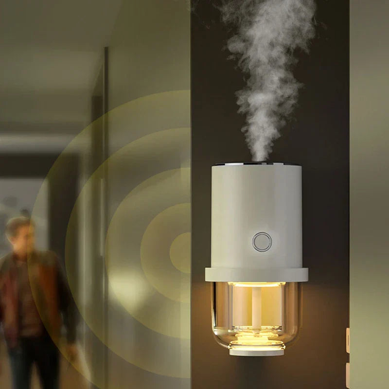 humidificador - dispositivo blanco y transparente montado en la pared que emite niebla vertical, luz amarilla cálida en la sección inferior, persona al fondo desenfocada