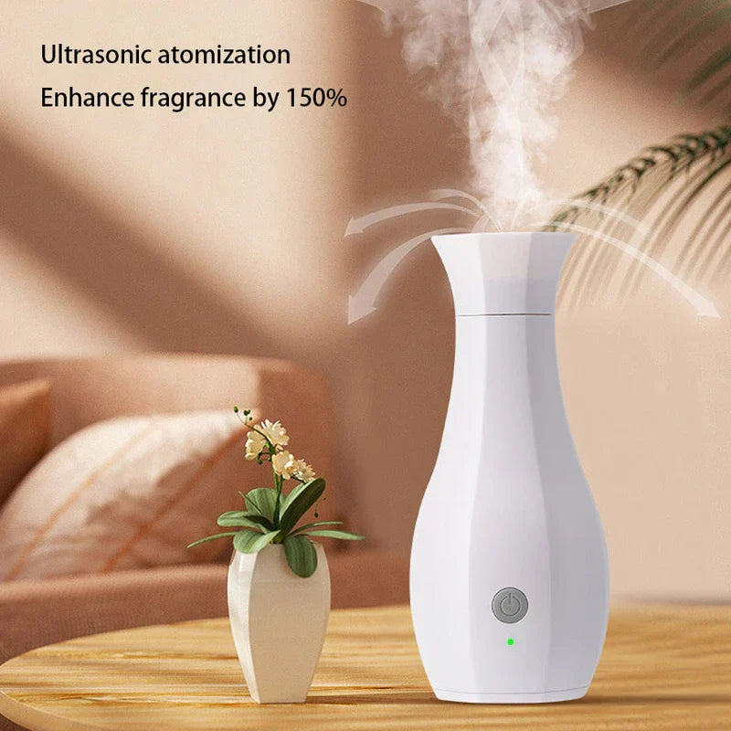 Máquina de perfume - Difusor blanco con forma de jarrón emite niebla sobre una mesa de madera, con un pequeño florero al lado y un sofá desenfocado al fondo