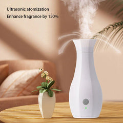 Máquina de perfume - Difusor blanco con forma de jarrón emite niebla sobre una mesa de madera, con un pequeño florero al lado y un sofá desenfocado al fondo