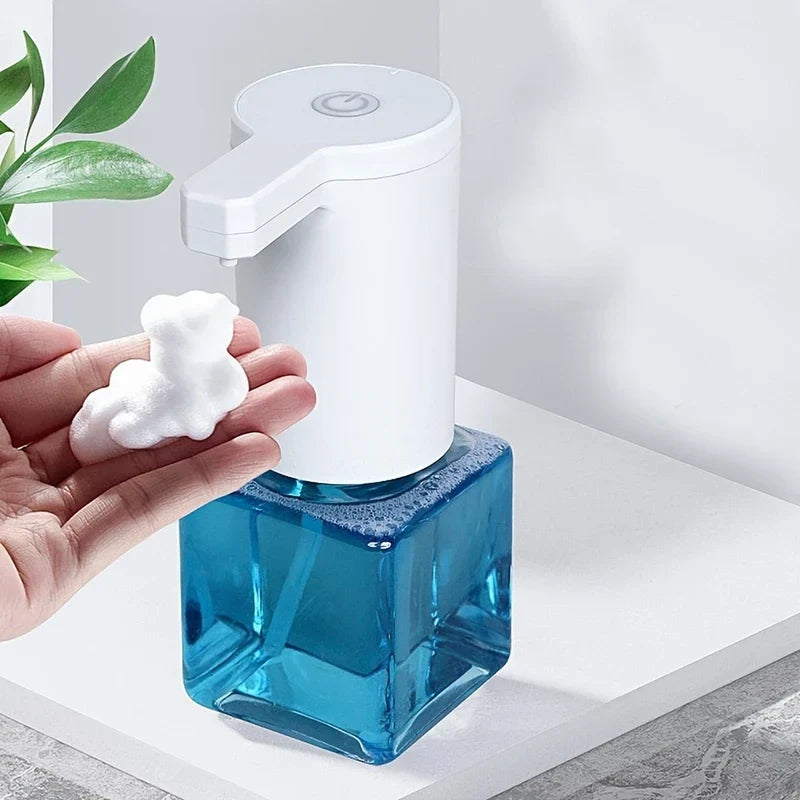 Soap Dispenser - Hand holding dollop of white foam under automatic pump on white countertop with green plant accent