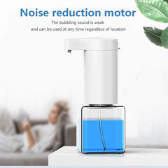 Automatic foam soap dispenser on white table, with text about noise reduction motor, blurred person on sofa in background