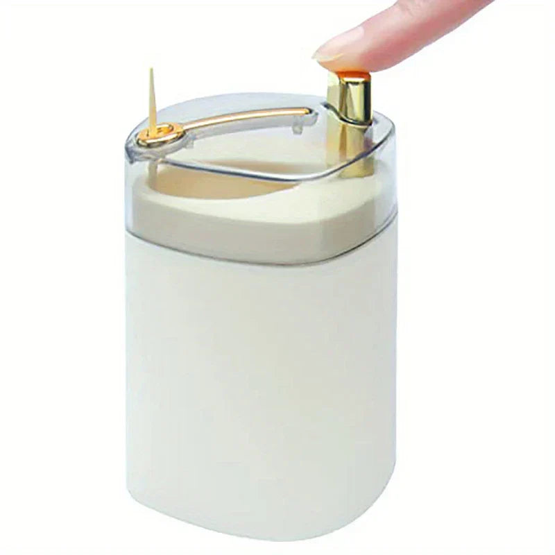 Toothpick Dispenser Holder - Finger pressing top button to dispense a single toothpick, cream body with gold accents and clear top