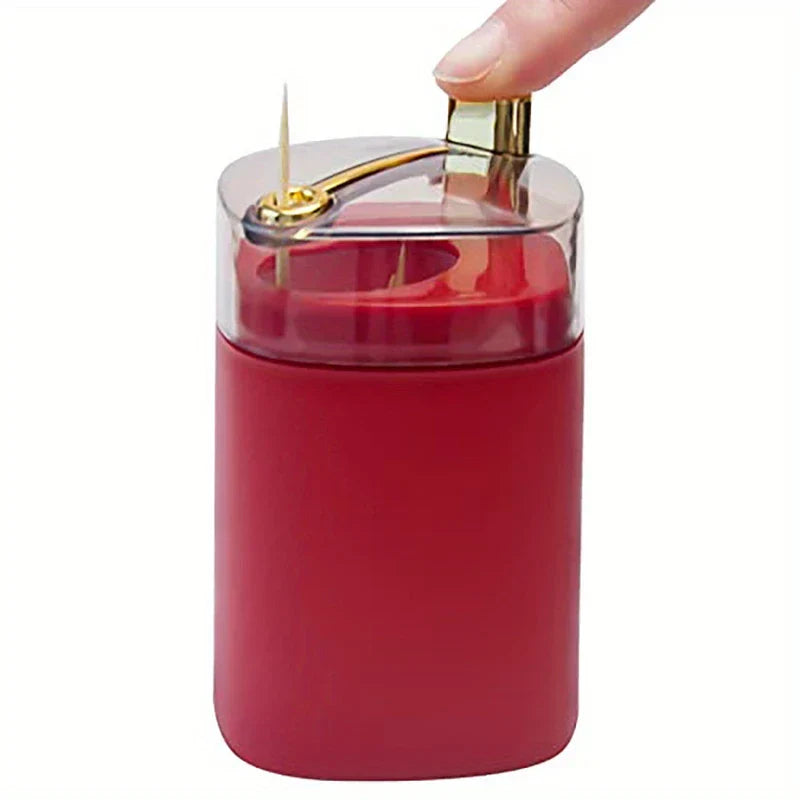 Toothpick Dispenser Holder - A thumb presses the gold top lever of a red toothpick holder with a clear lid, one toothpick protruding from the top.