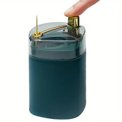 Toothpick Dispenser Holder - A thumb presses the gold top lever of a dark teal toothpick holder with a clear lid, one toothpick protruding from the top.