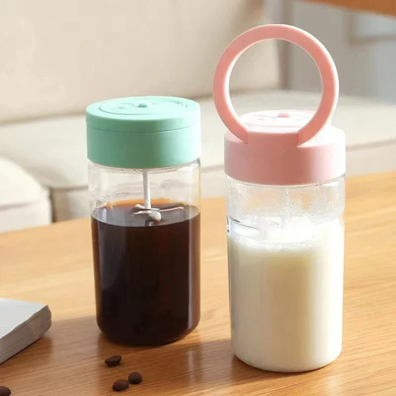 Automatic Mixing Mug - Two self-stirring cups on a wooden table, one mint green with dark liquid, one pink with milk, plus scattered coffee beans and a small notebook