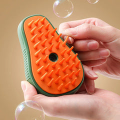 Pet Grooming Brush - Two hands holding a green and orange teardrop-shaped brush, one finger touching a silicone bristle