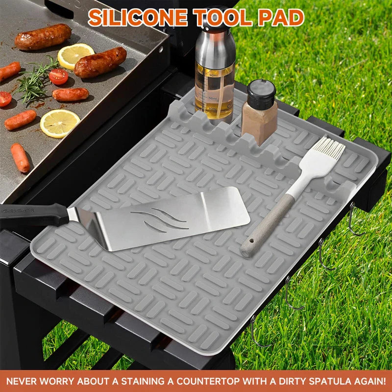 Bbq Grill Tool Rest Mat - Gray silicone tool pad on a black grill side shelf holding a spatula, basting brush, oil bottle, and spice shaker