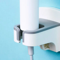 haartrockner ständer - Ein weißer zylindrischer Gegenstand, der in einem Badezimmer-Haartrocknerhalter platziert ist, mit einem grauen Kabel, das unten herabhängt.