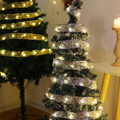Battery Box - Lit silver LED ribbon string light wrapped around small flocked Christmas tree with larger tree in background